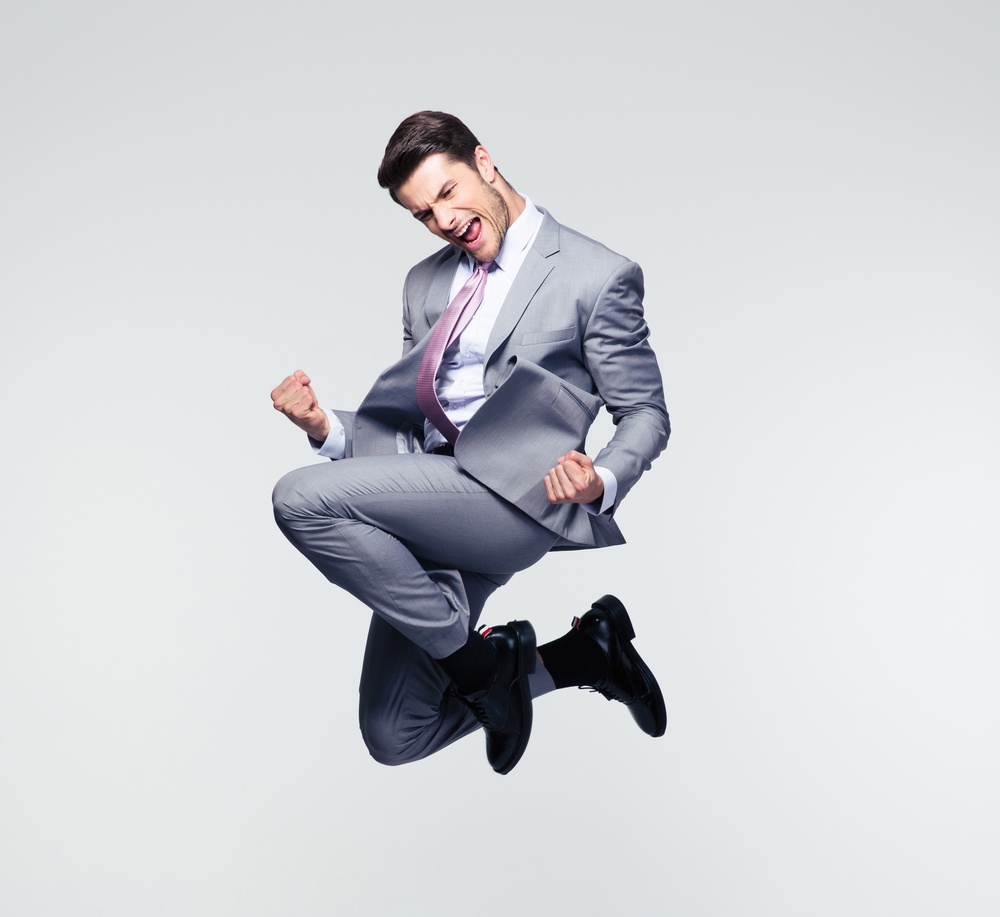 Funny cheerful businessman jumping in air over gray background.jpeg