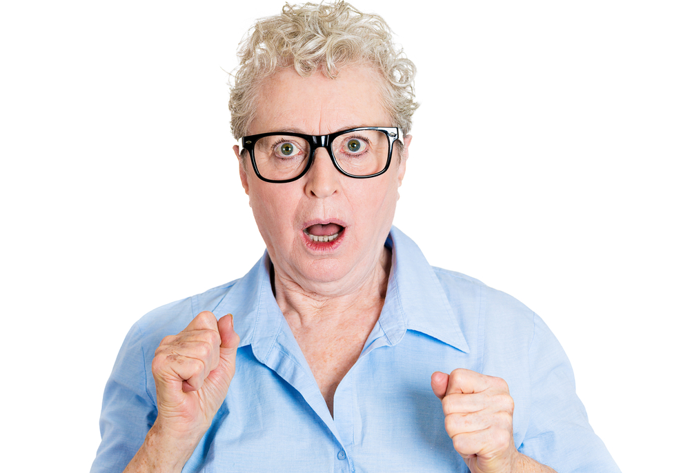 Closeup portrait, senior mature, nerd business woman in black glasses looking shocked, fists in air, isolated white background. Negative human emotions, facial expressions, feelings, reaction