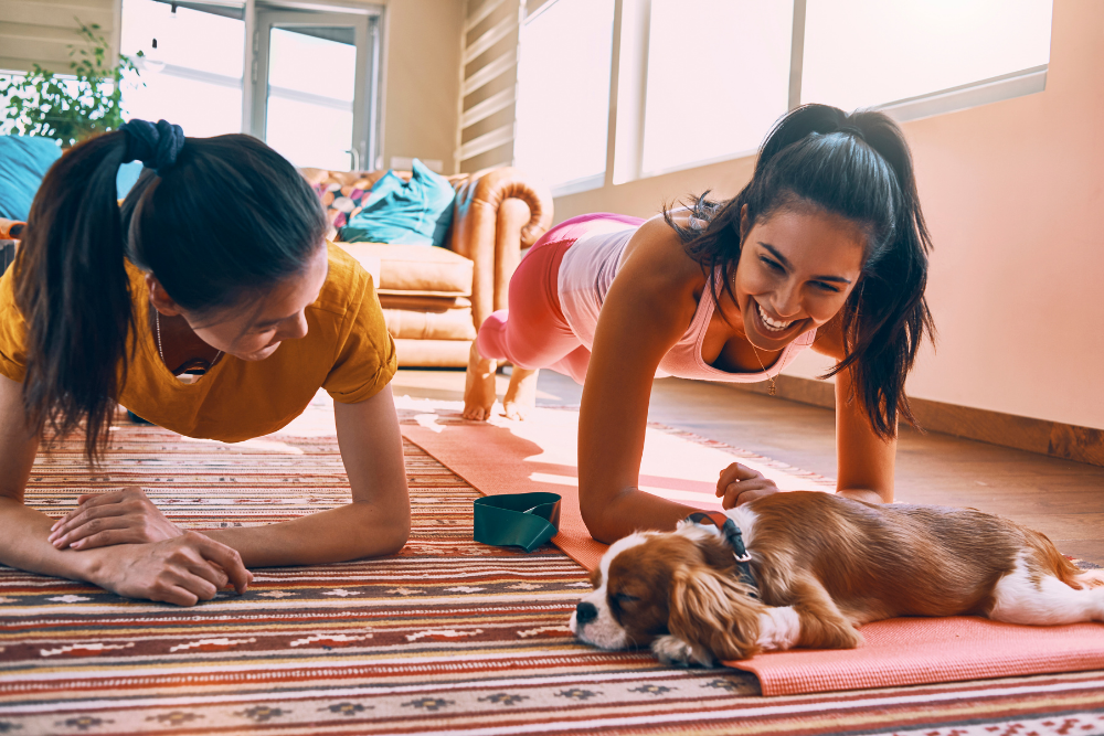Two women working out on yoga mats in living room with a dog 