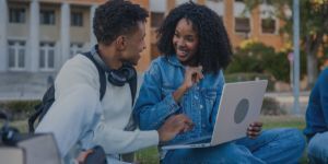 Students collaborating on laptop, smiling in university campus